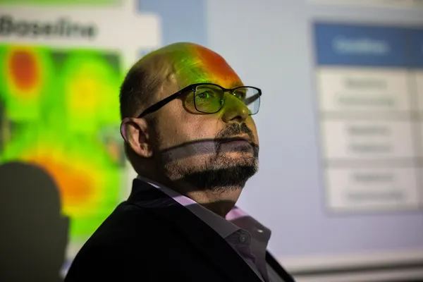 Quinlan influencer Dinco Bacic looks toward his audience as a multi-colored presentation slide is projected on the screen behind and also appearing slightly on his face.