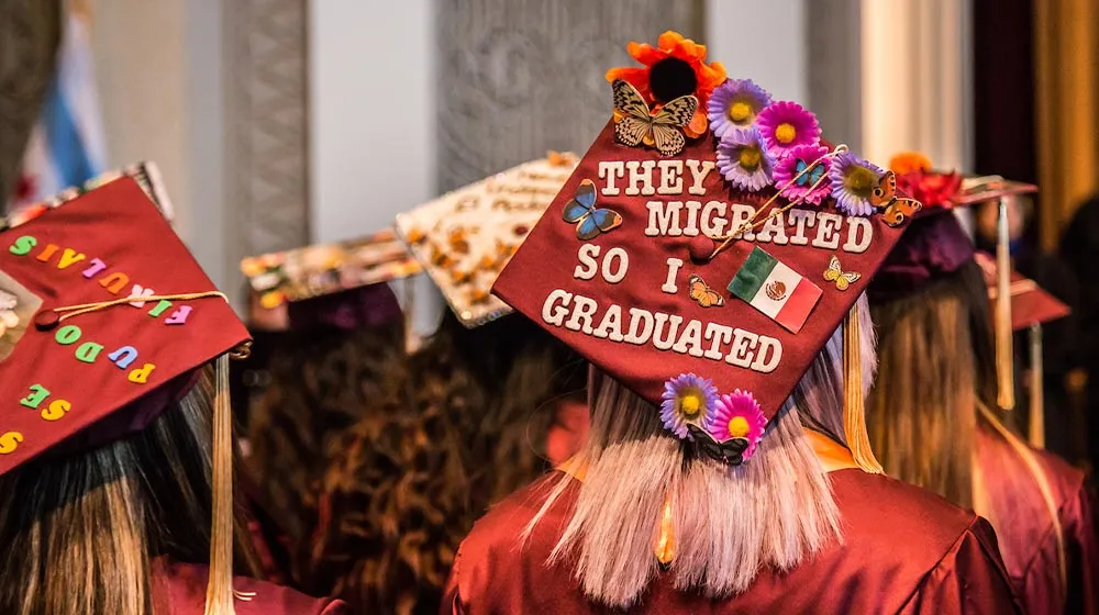 A maroon graduation cap decorated with flowers, butterflies, a Mexican flag, and the message 