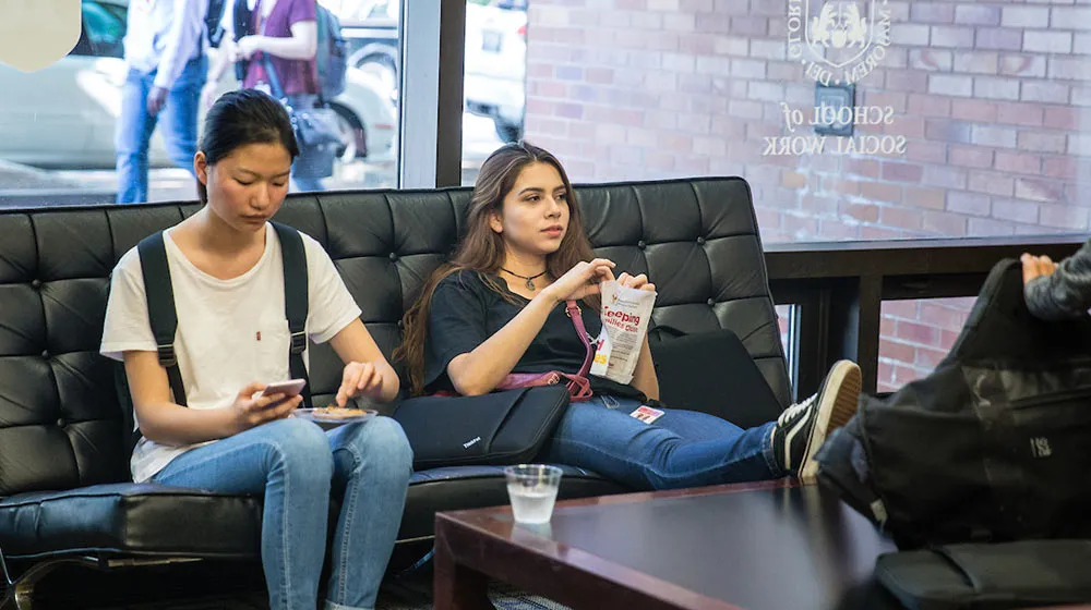 Two students relaxing on a black leather couch in the School of Social Work lobby at the Water Tower Campus.
