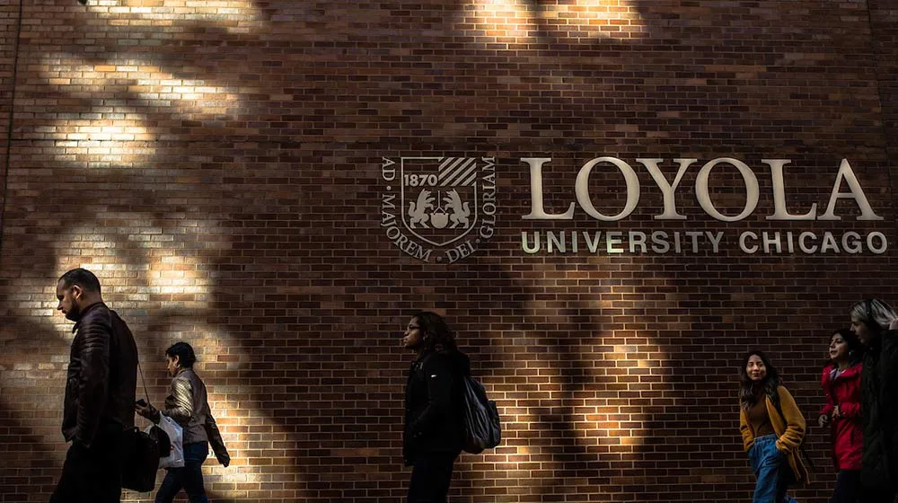 Students walking past a brick wall with Loyola University Chicago signage at Arrupe College