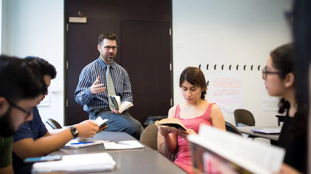 An instructor leading a seminar-style discussion with students as they read and reference books in a classroom at the Water Tower Campus.
