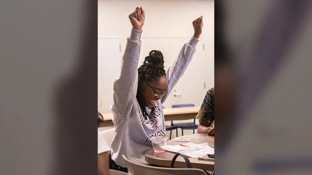 Excited student with arms raised in celebration while sitting at a table.