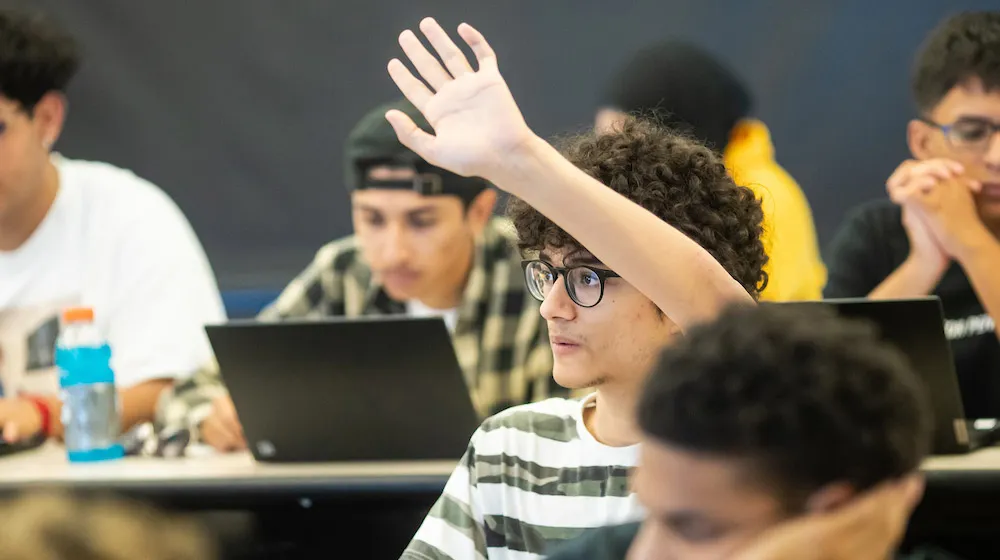 Students with hands raised during an interactive classroom discussion.