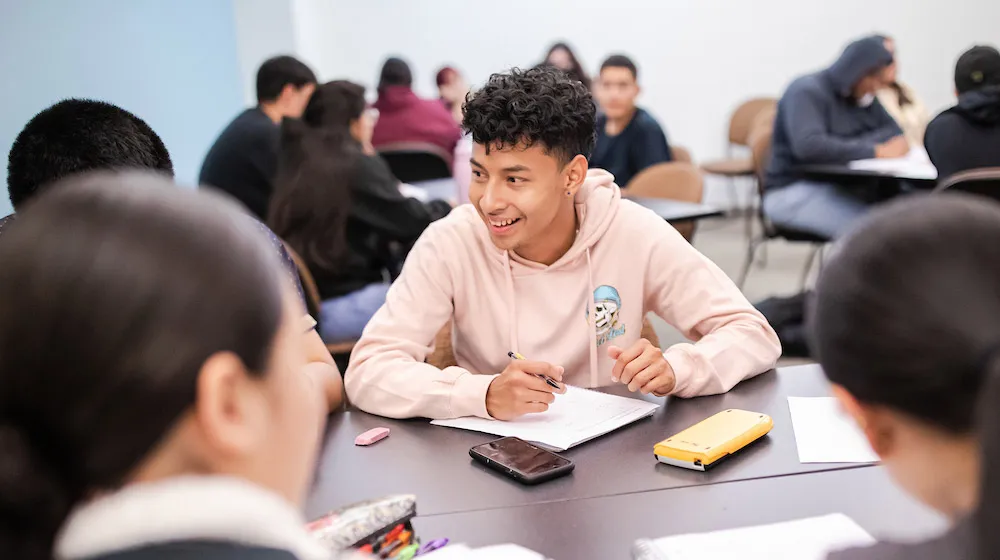 A smiling student in a pink hoodie talking with classmates during a study session in a classroom at the Water Tower Campus.