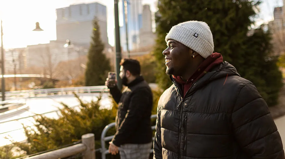 Smiling man in a beanie and puffer jacket at an outdoor skating rink.