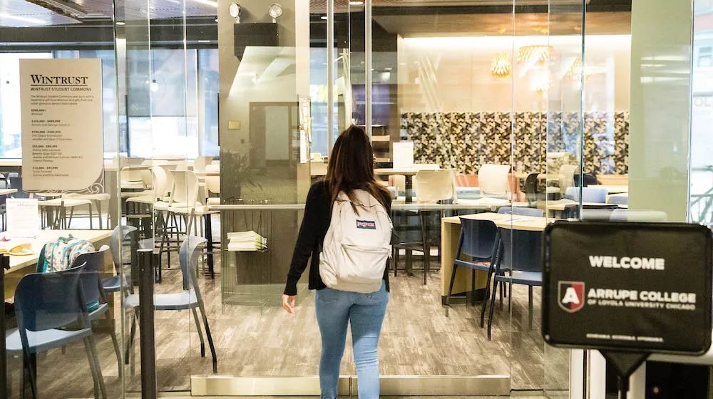 Student with a white backpack walking into the Arrupe College student commons.