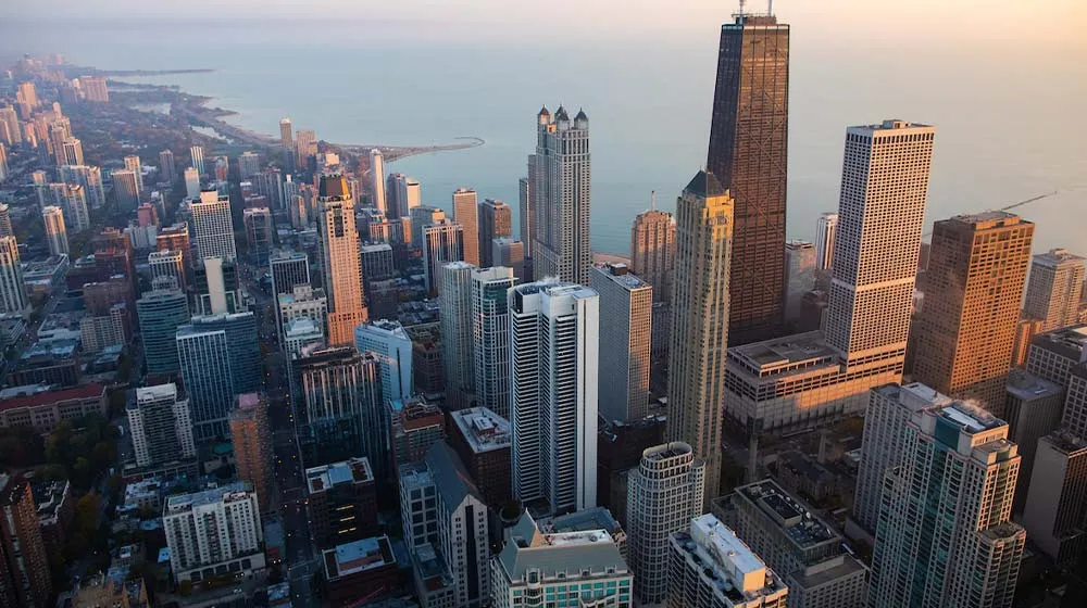 High-angle aerial view of the Chicago skyline at sunset, showing the Water Tower Campus area and 875 North Michigan Avenue against the Lake Michigan