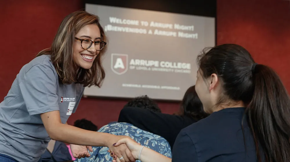 Smiling student shaking hands with a guest during Arrupe Night at the Water Tower Campus.