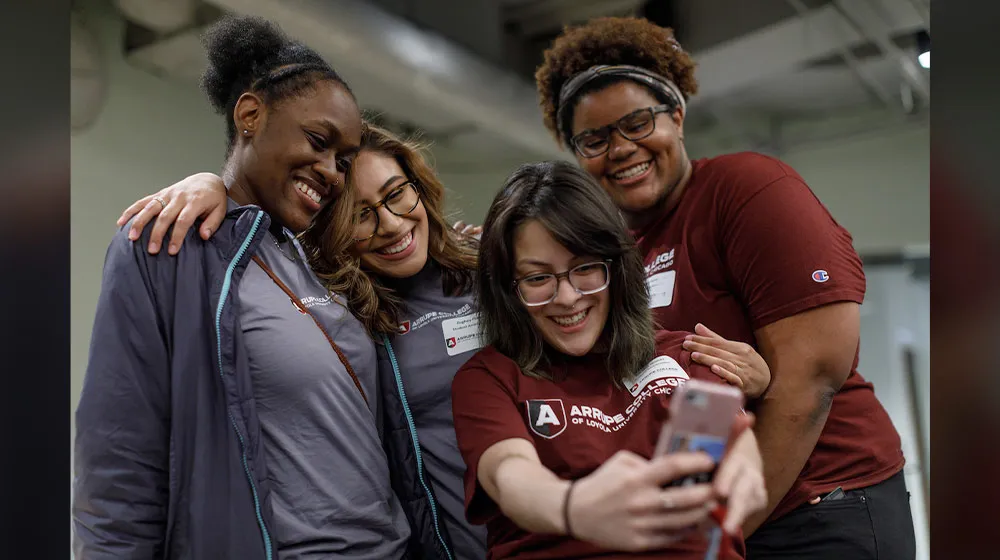 Four smiling Arrupe College students posing together for a selfie at the Water Tower Campus.