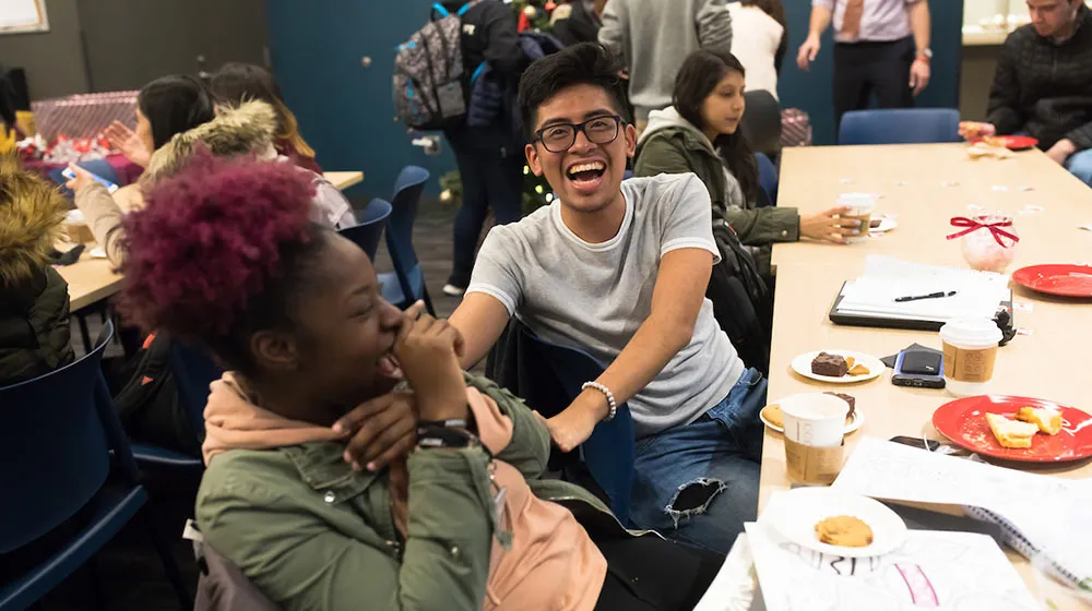 Students laughing and talking together at a table with snacks and coffee.