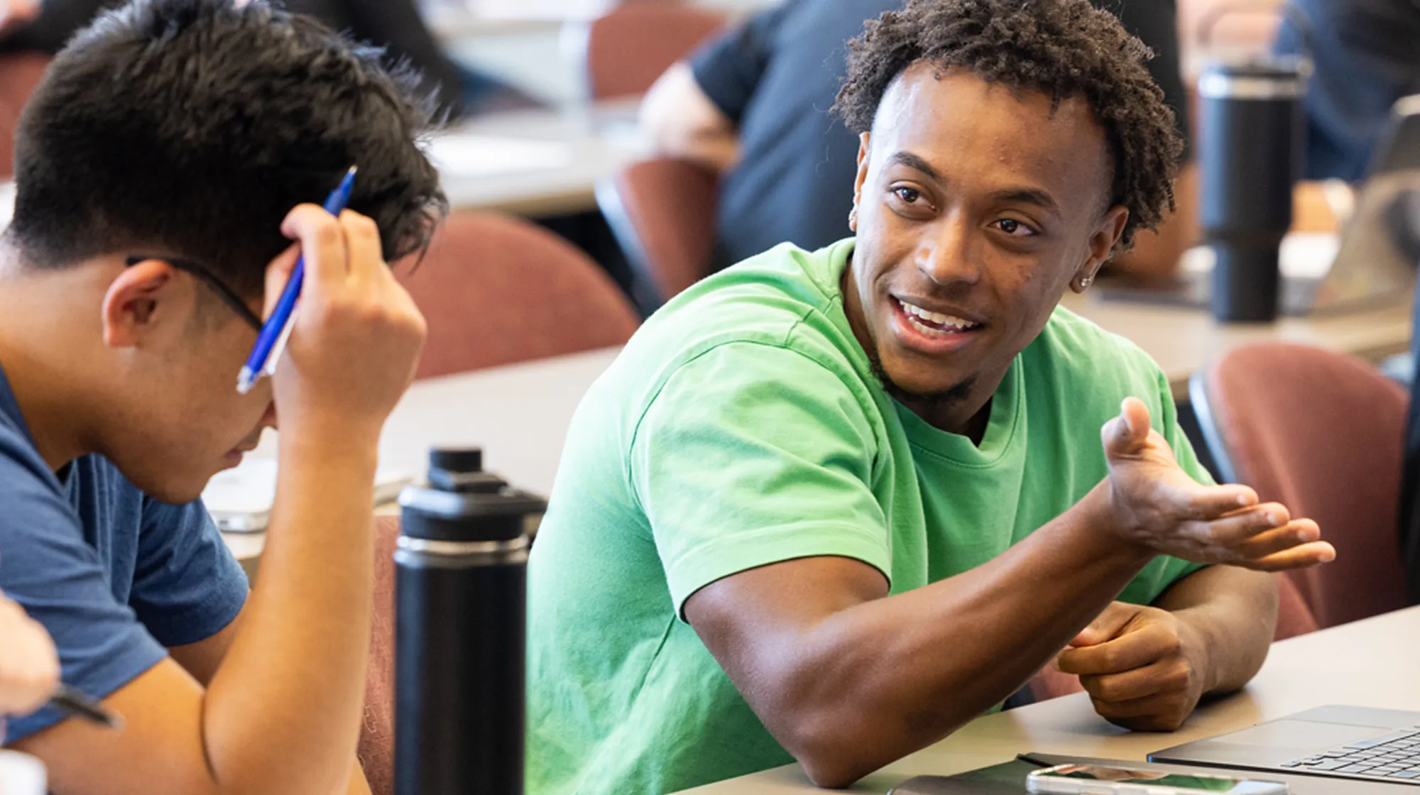 College students sitting together outdoors at a table, smiling and talking while studying.