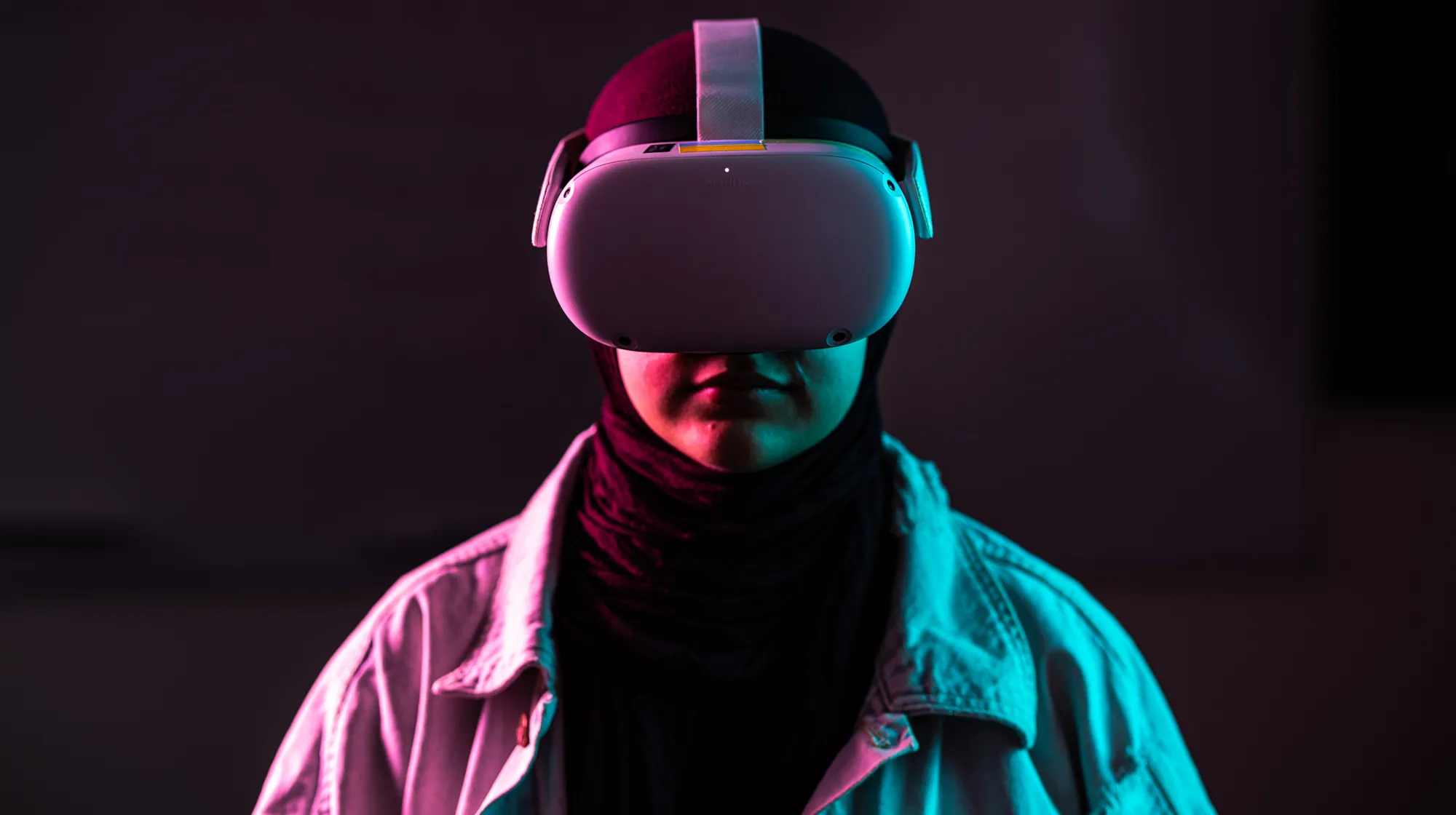 Person wearing a futuristic helmet and jacket, lit by neon pink and blue lighting against a dark background.