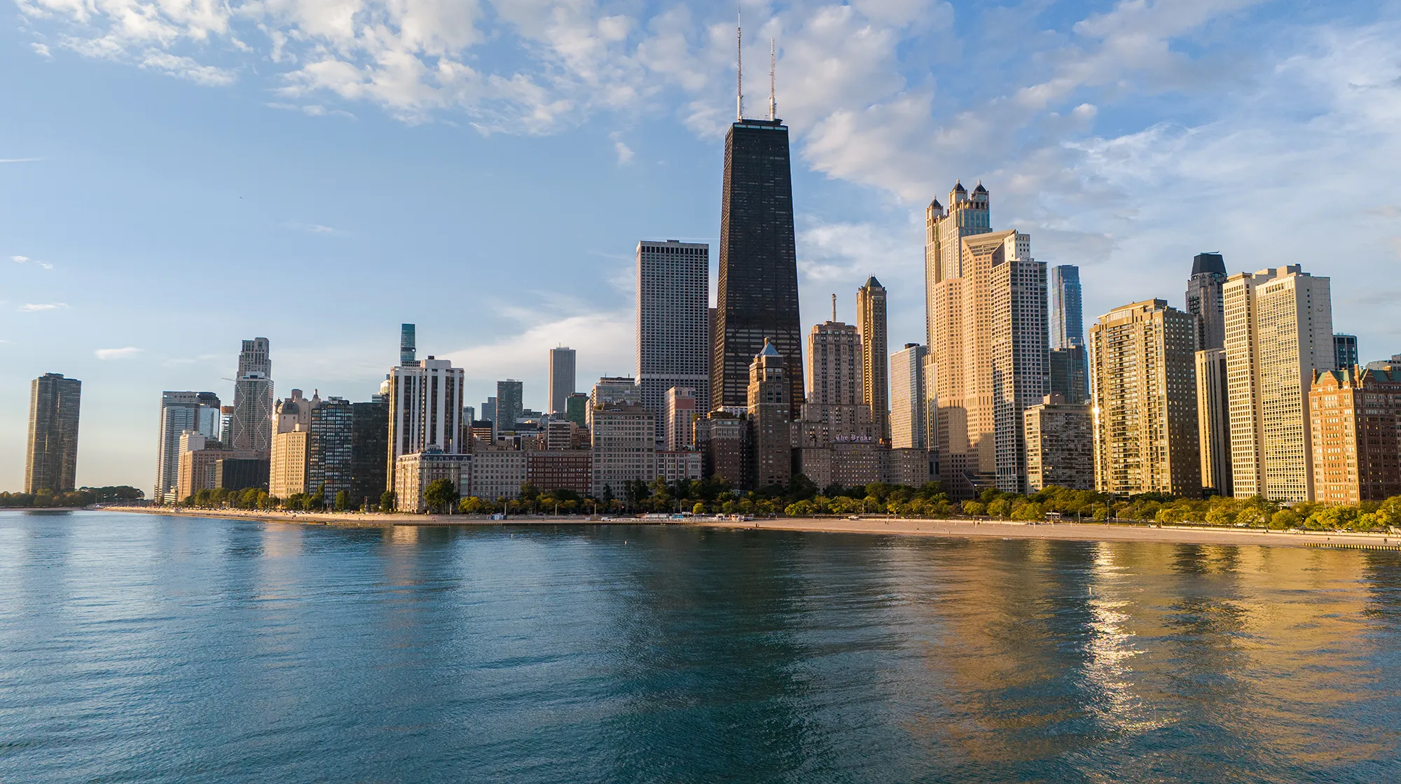 Chicago’s north loop buildings, including the John Hancock building, stand against a blue sky filled with white cumulus clouds