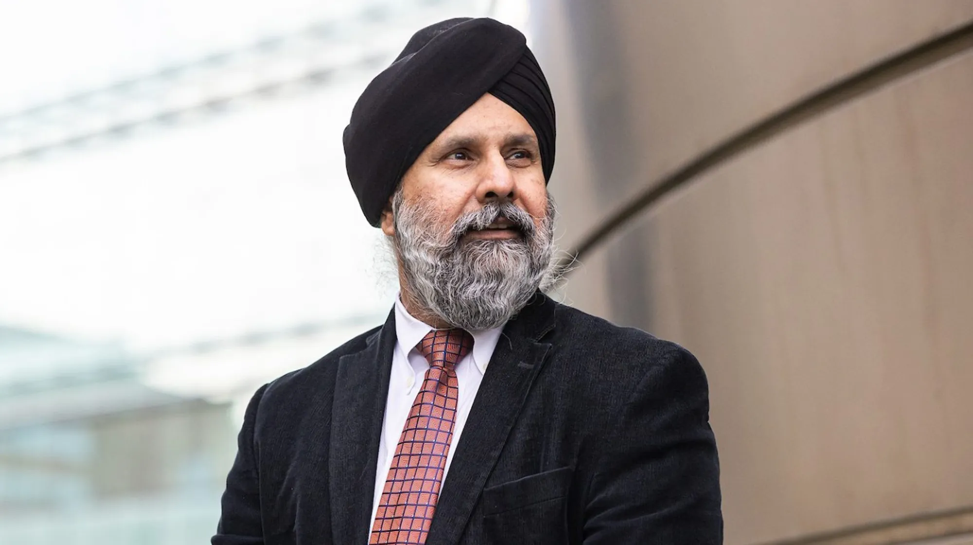 A man wearing a black turban, suit, and patterned tie, looking to the side