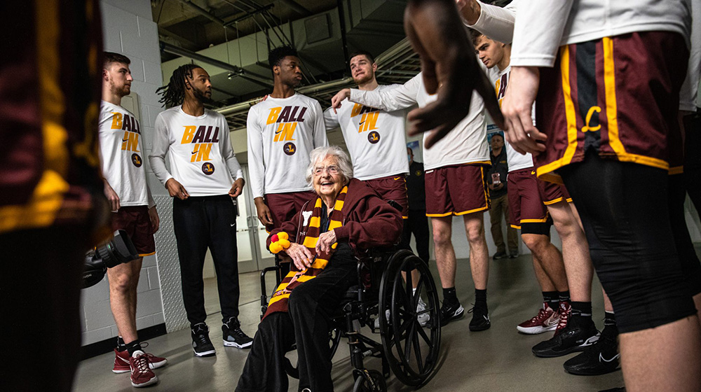 Sister Jean smiles as she sits in a wheelchair with Loyola University Chicago men's basketball players circled around her