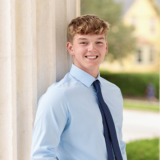 Portrait of a smiling student in business attire standing beside stone columns on Loyola University Chicago’s campus. Portrait of a smiling student in business attire standing beside stone columns on Loyola University Chicago’s campus.