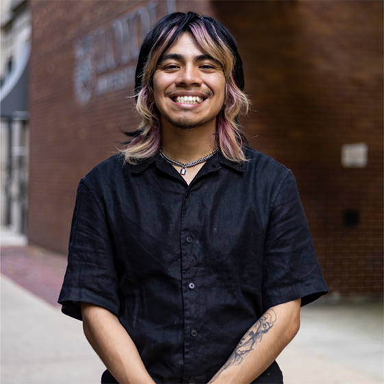 Portrait of a smiling student with multicolored hair wearing a black shirt on ��ݮ����’s campus.