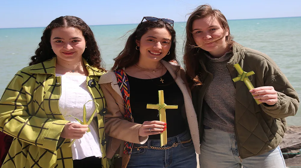 Three students holding palm leaf crosses