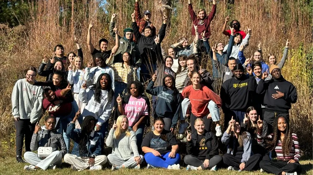 a group of students huddled together posing in the grass 