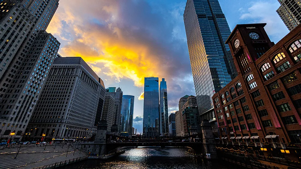 Downtown Chicago skyline at sunset with tall buildings reflecting golden light, viewed from a city street between high-rises.