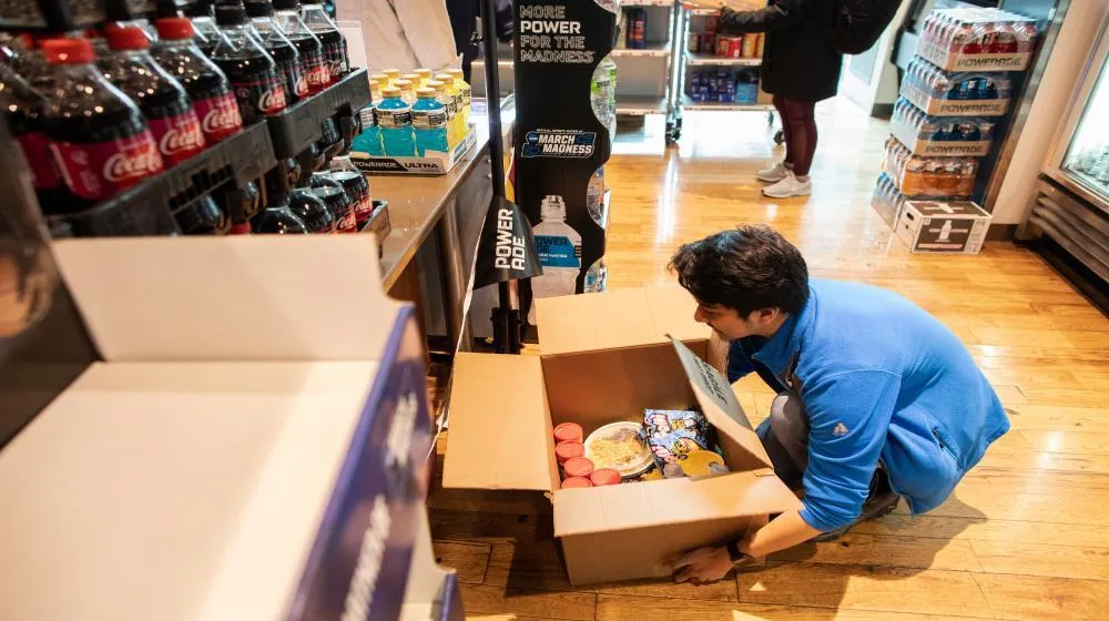 Man stooping to pick up a box of food via Loyola University Chicago's Food Assistance student resources. Man stooping to pick up a box of food via Loyola University Chicago's Food Assistance student resources.