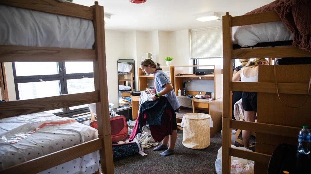 Student sorting clothes in a dormitory room via Loyola University Chicago's housing student resources. Student sorting clothes in a dormitory room via Loyola University Chicago's housing student resources.