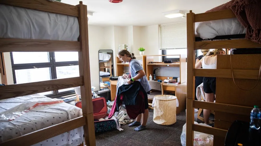 Student sorting clothes in a dormitory room via ��������Chicago's housing student resources.