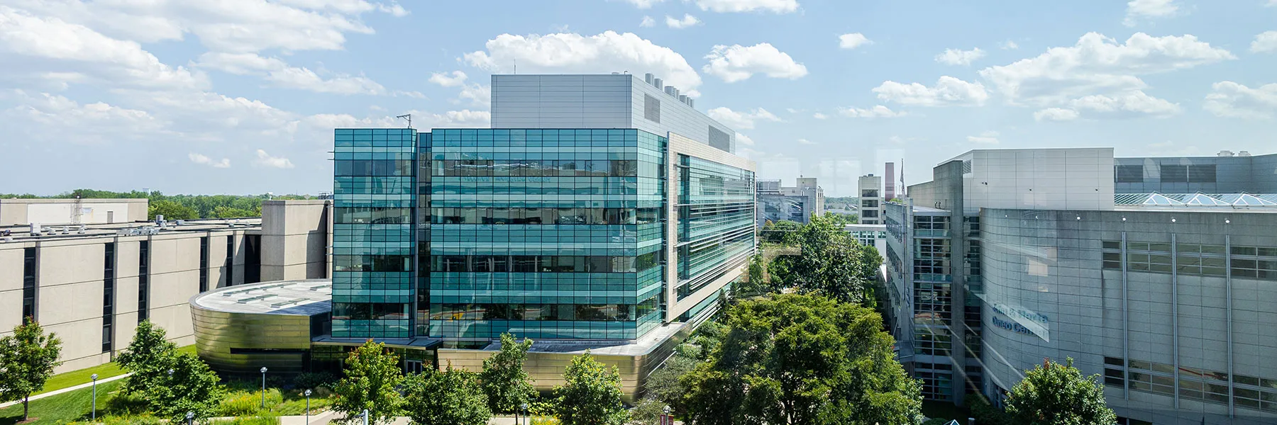 The Center for Translational Research and Education building on the Health Sciences Campus of Loyola University Chicago. It's a very clear day with bright white cumulus clouds in a light blue sky.