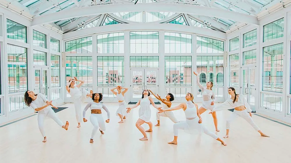 Сандра Кауфманн, сидящая у зеркальной стены, наблюдает за танцующими студентами рядом с ней.