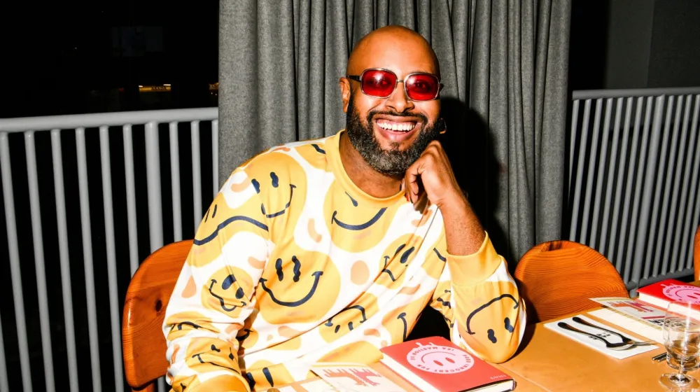 Ira smiles at the camera. Ira is sitting at a table with his book. 
