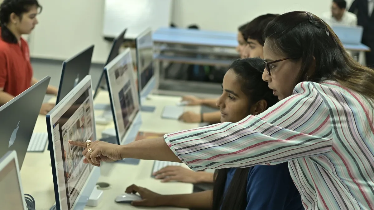 A student sits in front of a computer while an instructor offers guidance