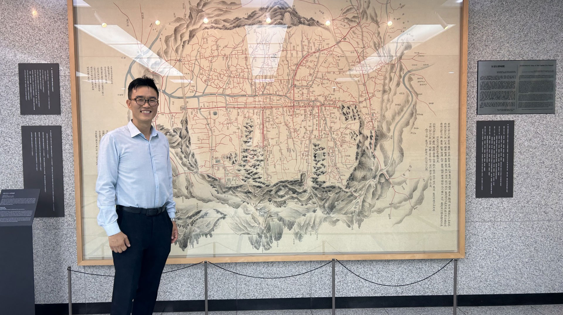 Seungho Moon standing in front of a wall map Seungho Moon standing in front of a wall map