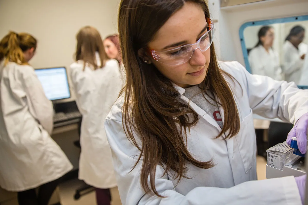 A large group of people gather for a photo in front of a statue. The people are all wearing yellow scarves with writing on them