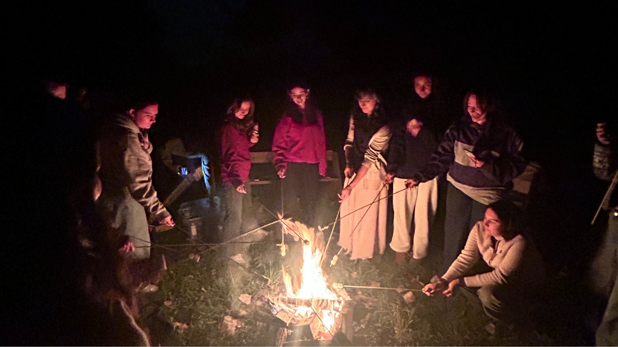 Gannon Scholars stand around a fire roasting marshmallows Gannon Scholars stand around a fire roasting marshmallows