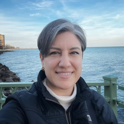 Emily Cain wears a black coat and smiles in front of a lake.