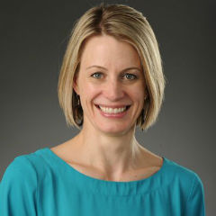 Dr. Christiana Zenner smiles in a blue shirt in front of a gray background.