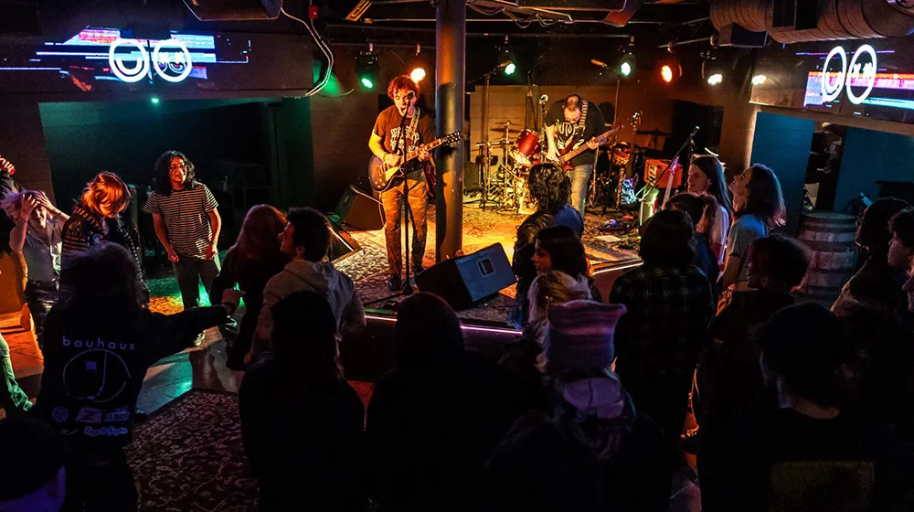 A guitarist plays onstage at a Chicago music venue as the audience watches