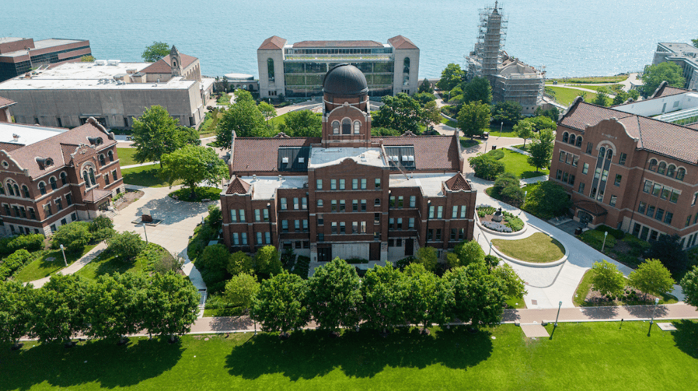 Aerial view of Loyola’s Lake Shore Campus, with Cudahy Library, green lawns, and Lake Michigan in the background.
