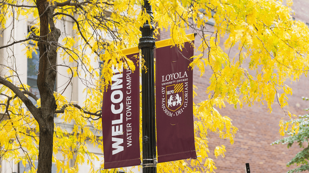 Maroon “Welcome Water Tower Campus” banners hang amid bright yellow autumn leaves.