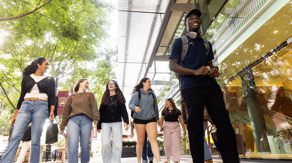 A group of students walks together, smiling, near Loyola’s Water Tower Campus on a sunny day.