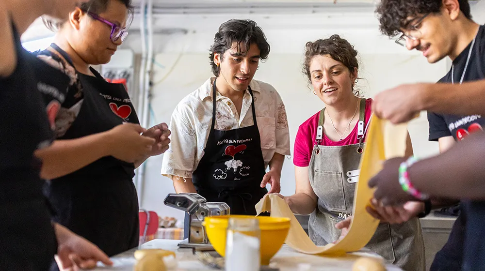A group of Loyola students standing around a table with bowls and pasta making ingredients on top of it as they experience making pasta together