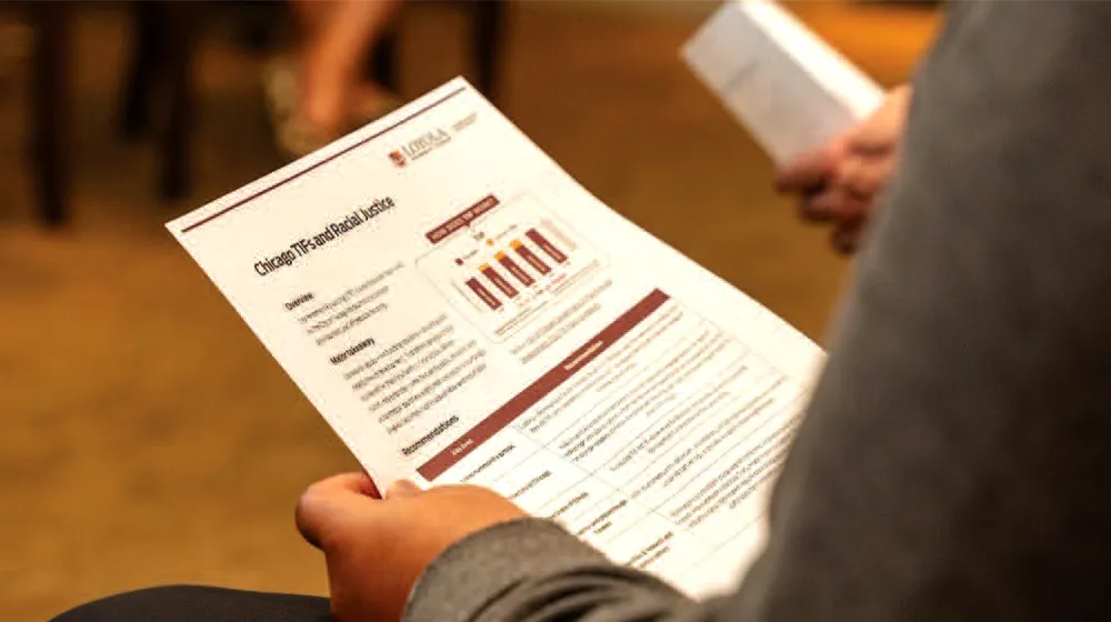 Person holds printed report showing charts and text while reviewing policy information during indoor meeting or training session setting.