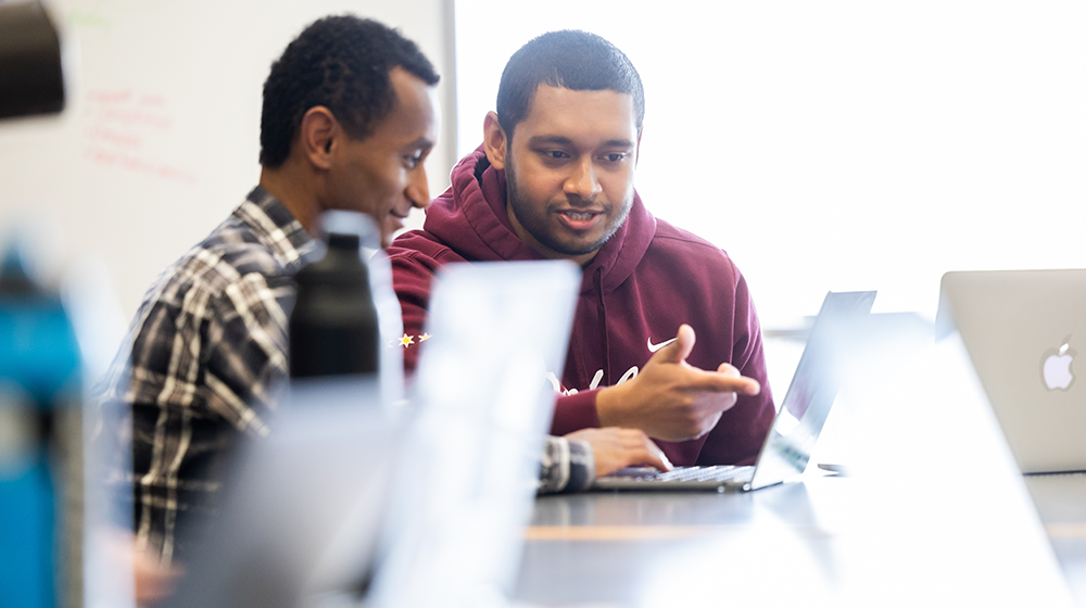 A student or faculty receives technology support from staff member while working on a laptop in a classroom or office.