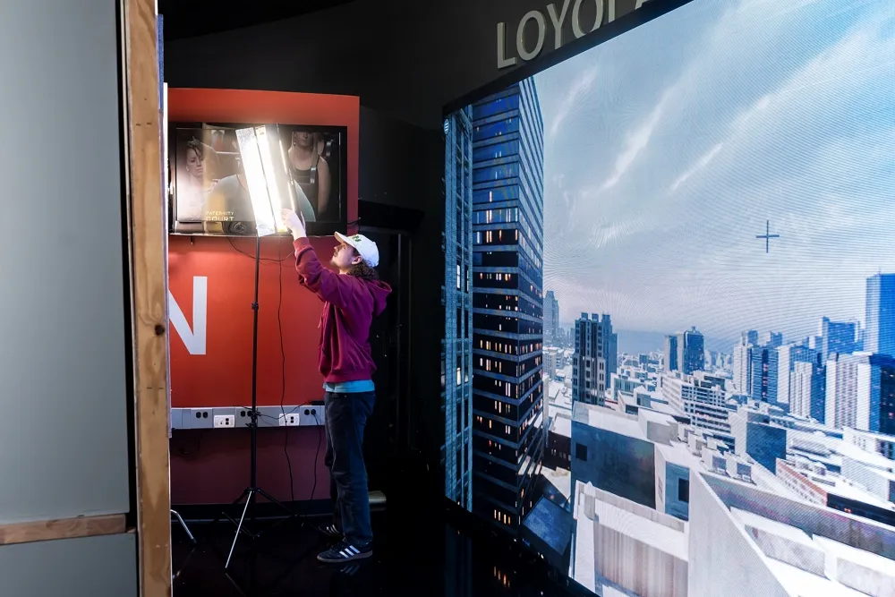 A student adjusting a light in front of a large LED digital wall display.