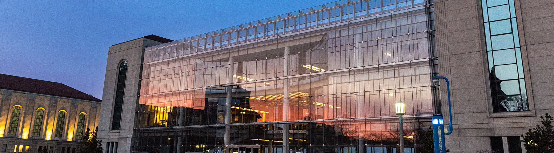 A gold and orange sunset reflects in the glass facade of the Information Commons building on the Lake Shore Campus.