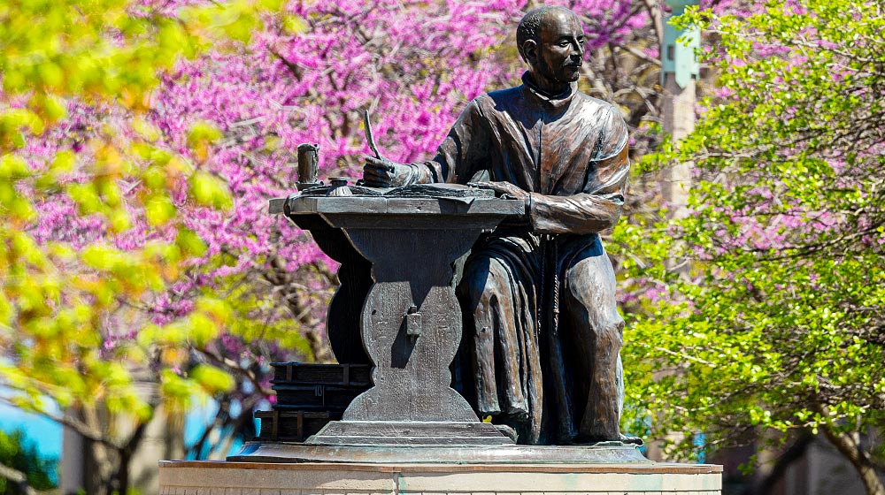 Statue of St. Ignatius of Loyola sitting at a desk