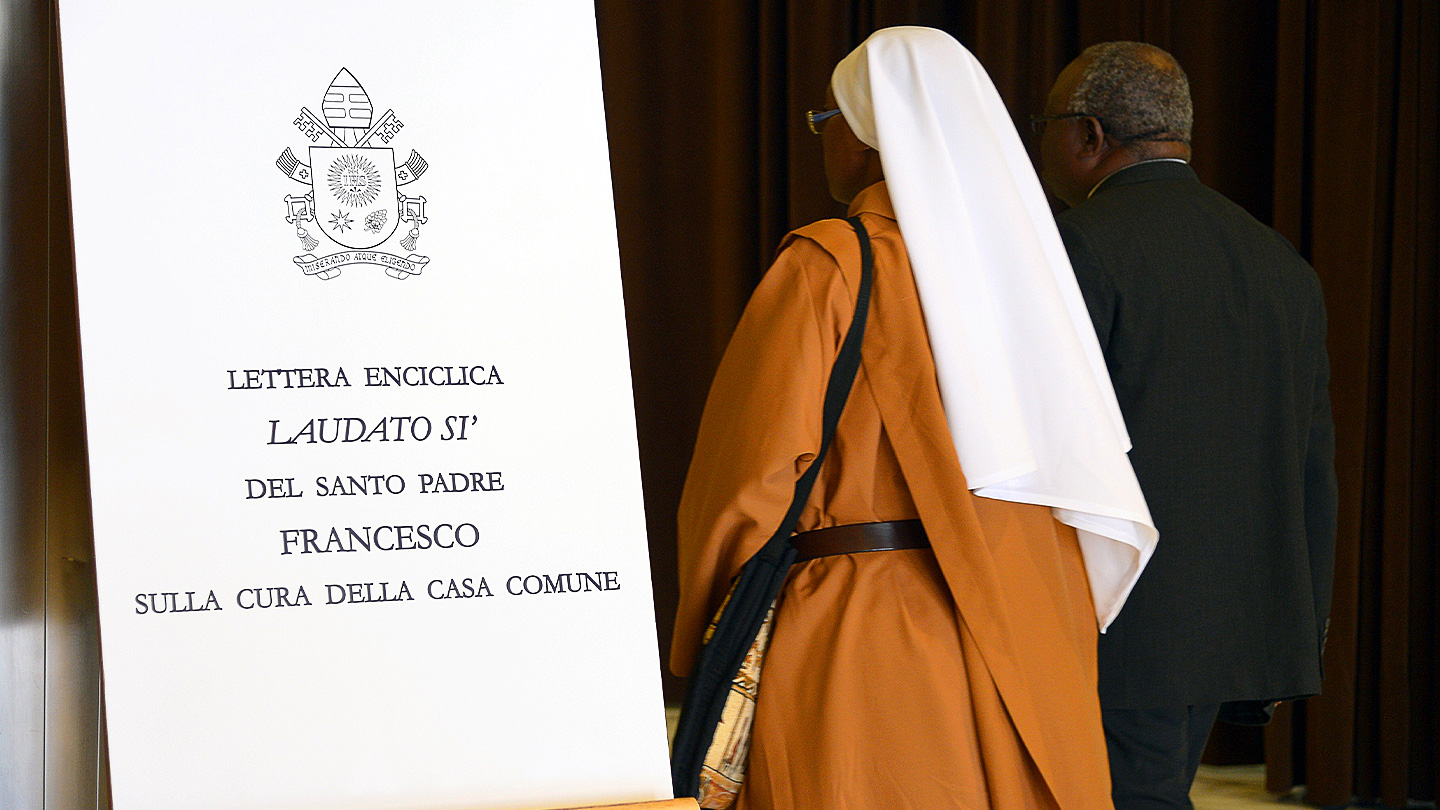 A religious woman in a habit standing next to large copy of St. Francis's encyclical letter 
