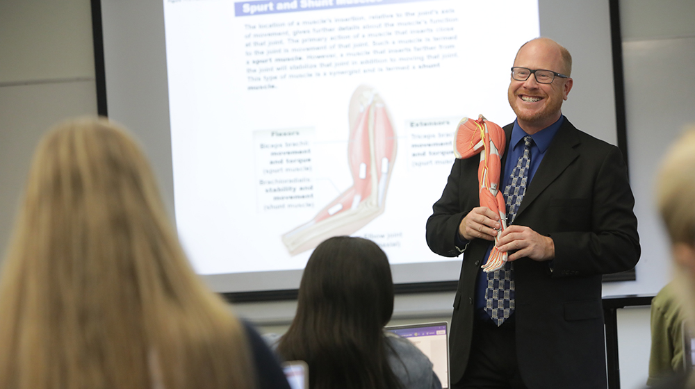 Matt Bruder holds a model arm in front of a classroom Matt Bruder holds a model arm in front of a classroom