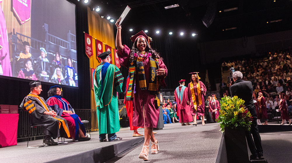 A CARE Pathway graduate walks across the stage at Commencement with arms raised