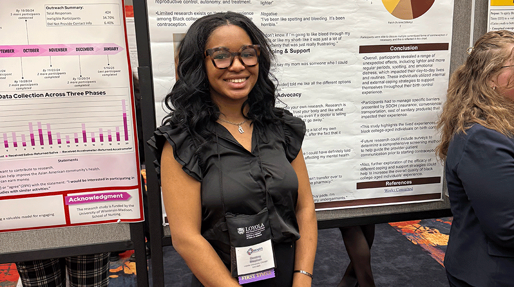 Undergraduate Destiny Stephen stands in front of research posters and smiles. 